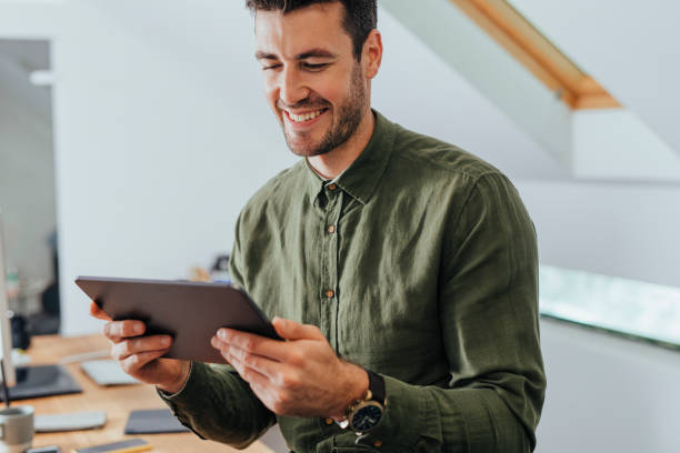 istock Smiling Man in a Green Shirt Using a Digital Tablet PC in the Office 1295653966
