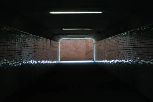 The exit of a pedestrian tunnel, an underpass, leads to a brick wall.