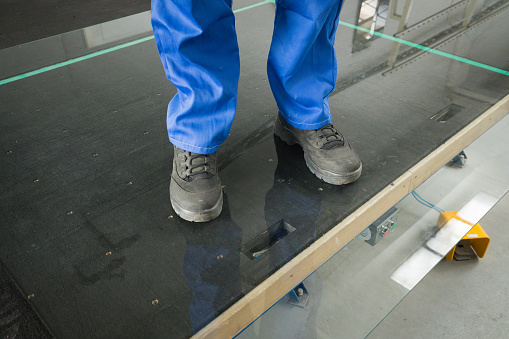 The worker is standing on a pane of thick glass. Durable, thick tempered glass