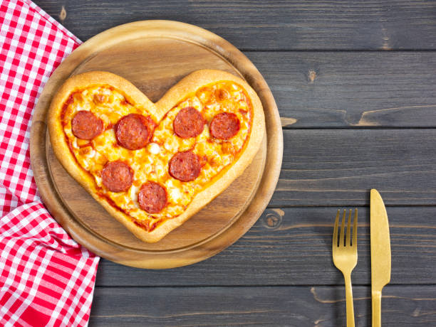 istock Heart shaped pizza. Pizza pepperoni on cutting board with fork and knife. 1295659376