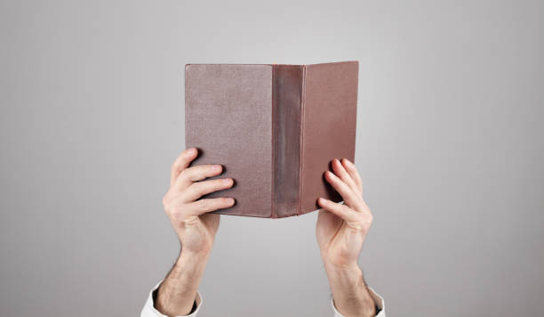 istock Male hands holding book on grey background. 1295662871