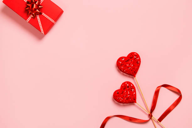 istock Abstract composition with two decorative hearts and red present box on pink paper background. 1295663634