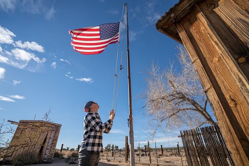 Young man hoisting American flag against blue sky