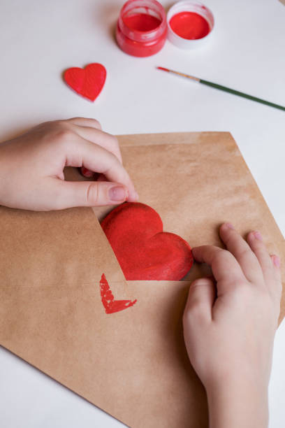 istock The child puts a decorative heart painted with red paint in an envelope. 1295665884