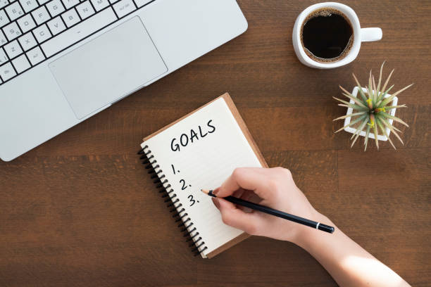 istock hand is writing goals in a notebook. new year resolutions and plan. Top view word goals on notebook with laptop and coffee. 1295667688