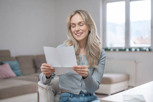 istock Young woman smiling while reading a letter at home 1295669624