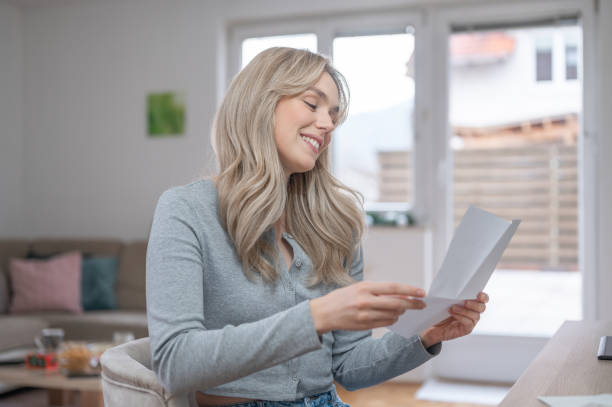 istock Young woman smiling while reading a letter at home 1295669653