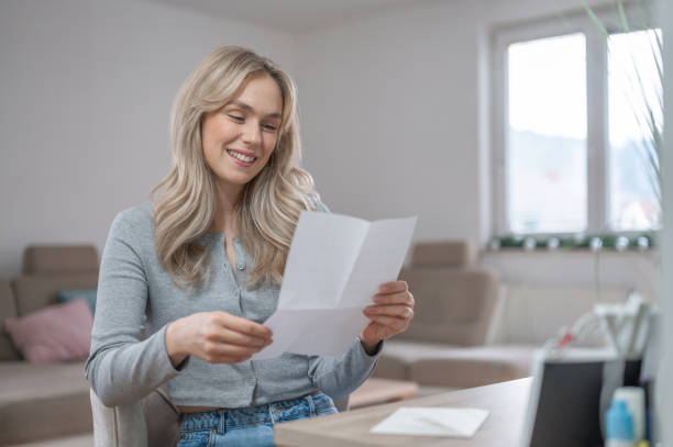 istock Young woman smiling while reading a letter at home 1295669661