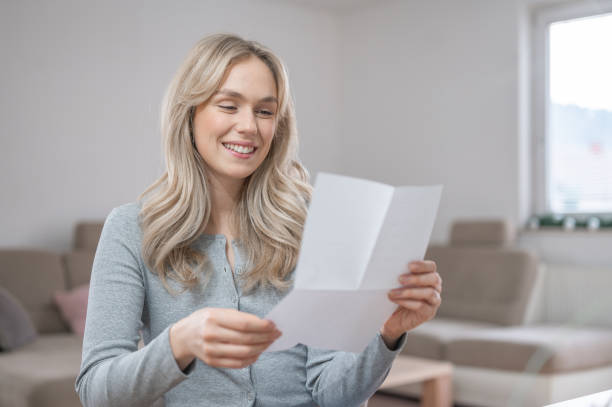istock Young woman smiling while reading a letter at home 1295669674