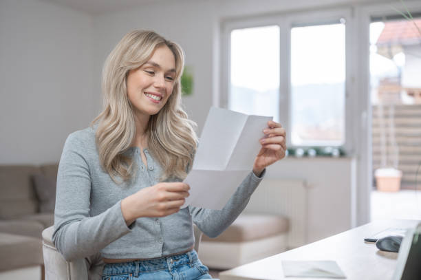 istock Young woman smiling while reading a letter at home 1295670029