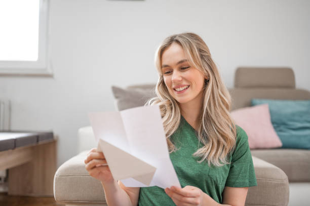 istock Young woman smiling while reading a letter at home 1295670192