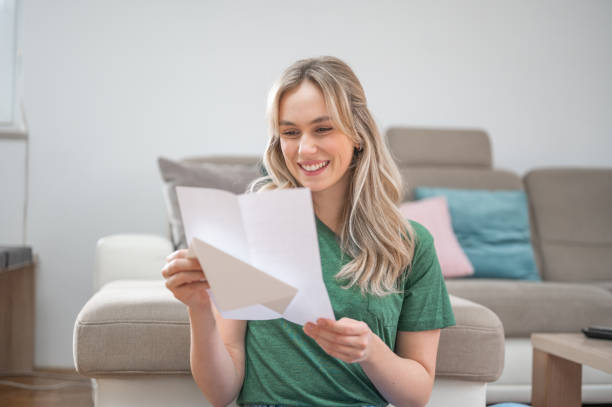 istock Young woman smiling while reading a letter at home 1295670239