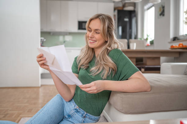 istock Young woman smiling while reading a letter at home 1295670298