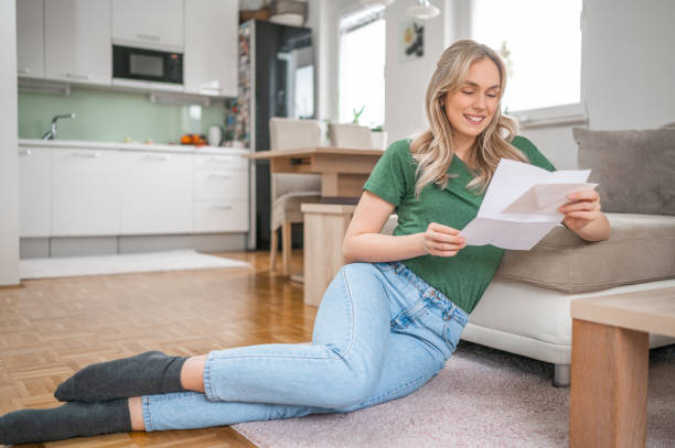 istock Young woman smiling while reading a letter at home 1295670299