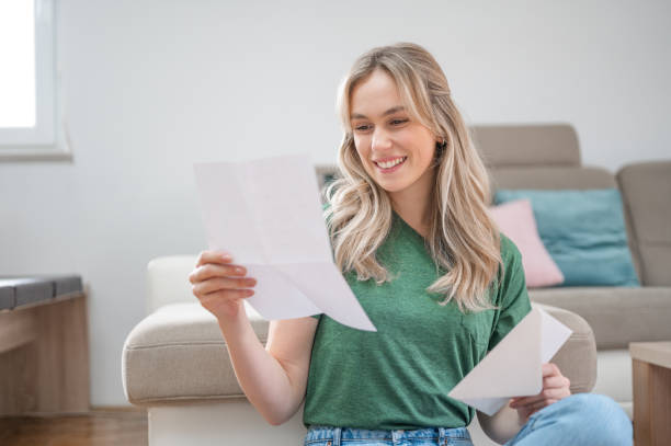 istock Young woman smiling while reading a letter at home 1295670335