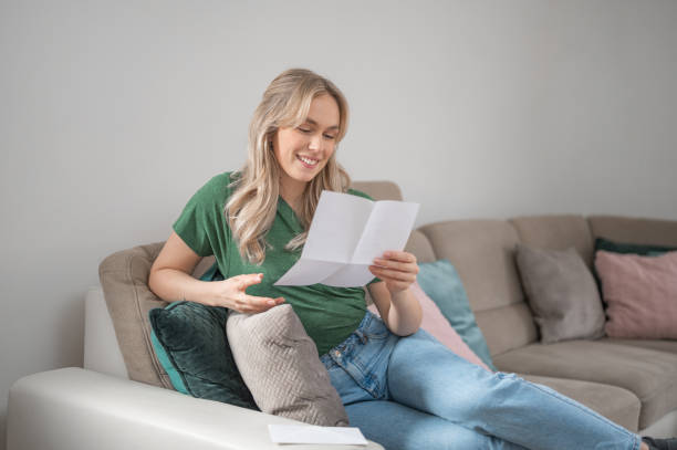 istock Young woman smiling while reading a letter at home 1295670365