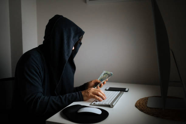 istock Man Wearing Hooded Shirt And Mask Using Laptop In Dark To Hack 1295676368