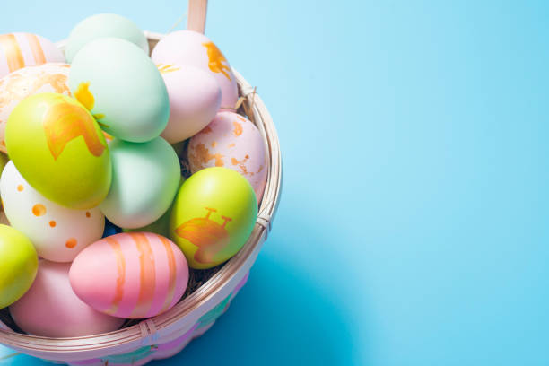 Easter basket filled with painted Easter Eggs over a blue background. Colorful painted easter eggs in basket on blue background.