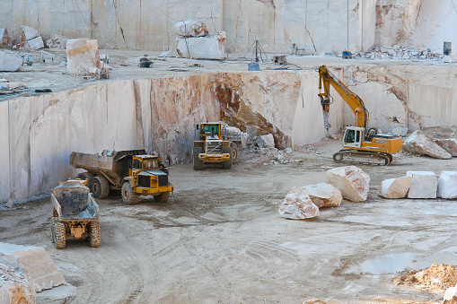 Construction vehicles working in marble quarry with oversized marble blocks
