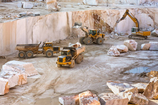 Construction vehicles working in marble quarry with oversized marble blocks Construction vehicles working in marble quarry with oversized marble blocks open pit mine photos stock pictures, royalty-free photos & images