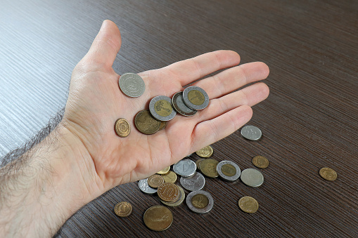 Male hand holding several international currencies coins with more on wooden background