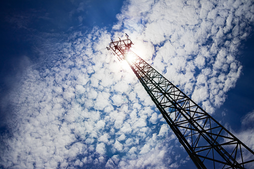 A very very tall telecommunication antenna with a bottom up angle view and an evident perspective from the ground, with a sunny day and blue sky background and lens flares