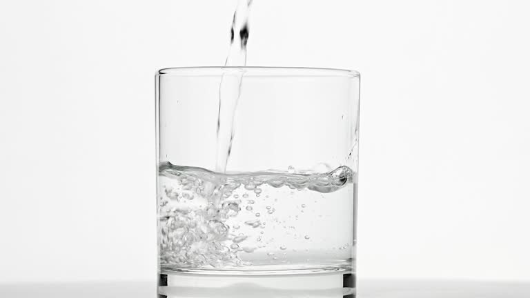 Pouring water in drinking glass over white