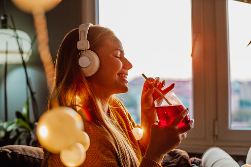 Young woman at home, drinking and listening music with headphones