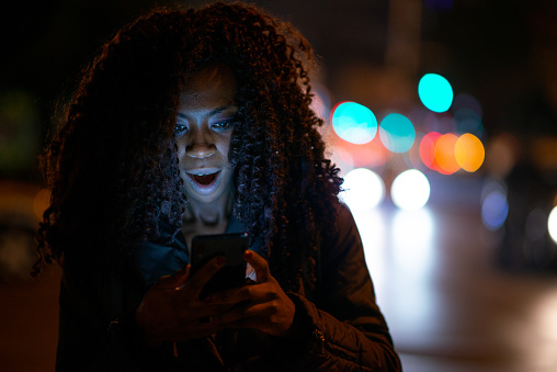 Portrait of a surprised woman reading bad news on her phone on street at night.