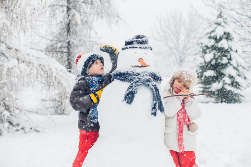 Boy and girl having fun outdoors and playing in the snow with snowman.