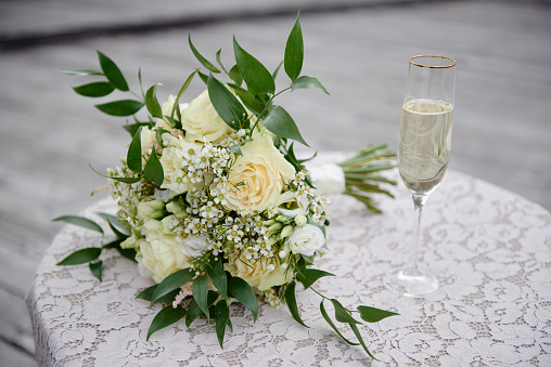 Close up of bridal bouquet and glass of champagne on white table outdoors, copy space. Wedding concept