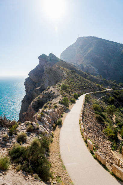 istock Scenic walking path along steep cliffs with backlight along the ocean in the natural park 'Serra Gelada' in Albir, Spain 1295695888
