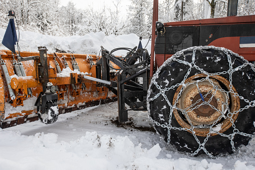 Snowplow on Tractor With Tire Chains in Winter Rural Scene.