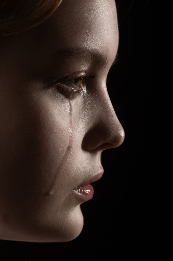 sad woman crying, looking aside on black background, closeup portrait, profile view