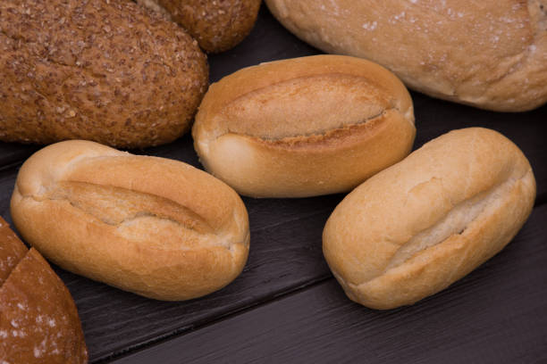 bakery - gold rustic crusty loaves of bread and buns on black chalkboard background top view - baked bread breakfast brown imagens e fotografias de stock