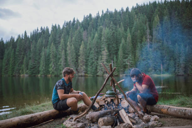 istock Two Young Male Friends Are Smiling And Chatting Next To The Campfire while drinking herbal tea 1295701235