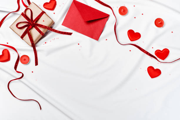 istock Romantic concept. Valentines day background. Red envelope, Gift box and hearts on white silk sheet 1295701447