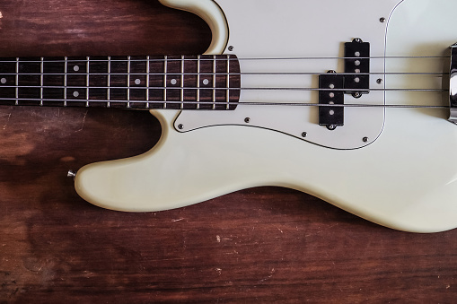 Close-up picture of a white, 5 strings bass guitar with pickup and fretboard on a black background