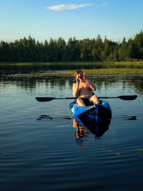 nastoletni chłopiec robi "wow" twarz z rękami na kajaku na małym jeziorze. - summer camp child teenager kayak zdjęcia i obrazy z banku zdjęć