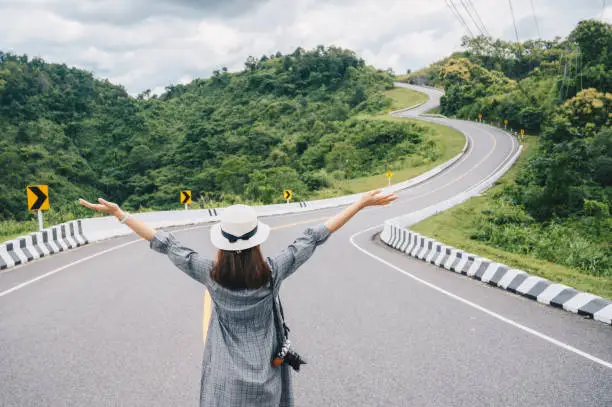 Photo of Asian tourist raised her hands while looking to beautiful steep curved road (look like number 3) on the high mountain in Nan province, Thailand.