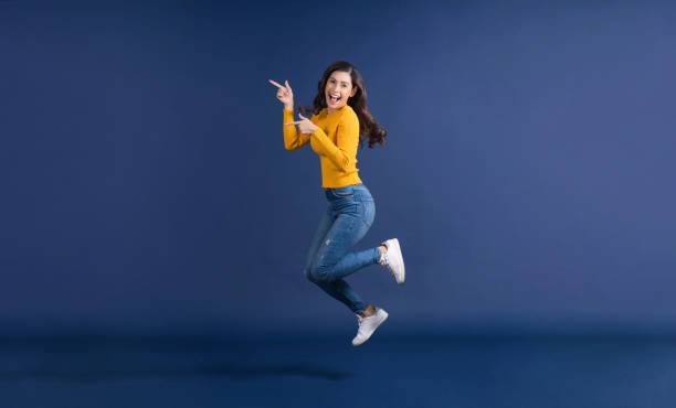 glückliche junge asiatische frau in bunten gelben farbe lässige kleidung springen und präsentieren - hochspringen stock-fotos und bilder