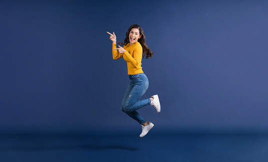 Feliz joven asiática en colorido color amarillo ropa casual saltando y presentando photo