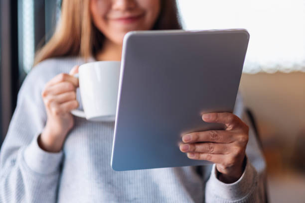 a beautiful young asian woman holding and using digital tablet while drinking coffee