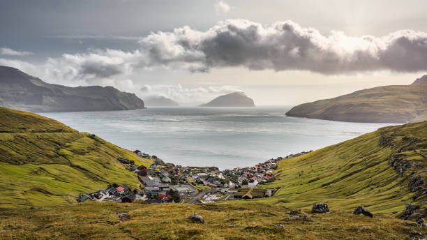 Kvivik Village Faroe Islands Fjord Streymoy Island Koltur Island Panorama View Faroe Islands Kvivik Village and Fjord Bay Panoramic View from above. View to the North Atlantic Ocean Canal between the Island of Vagar, Streymoy Island and Koltur Island. Coastal village of Kvivik between green grass covered fjord hills under dramatic sunny summer cloudcape on the west coast of Streymoy Island. Koltur Island in the center on the north atlantic horizon. View to Streymoy Island western coast on the left and Vágar Island coast on the right of the Panorama. Kvivik Village and Fjord Bay, Streymoy Island, Faroe Islands, Kingdom of Denmark, Nordic Countries, Northern Europe vágar photos stock pictures, royalty-free photos & images