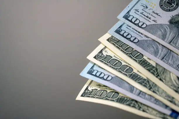Closeup of the bottom left corner of six hundred dollar bills, of variety of old and new print styles against a grey background.