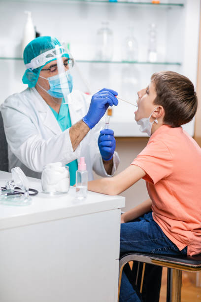istock Doctor in protective workwear taking sample from boy's mouth with COVID-19 testing kit 1295741197