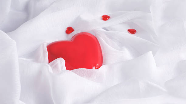 istock Valentine's day concept with red heart on a white background draped in white fabric, top view with copy space. 1295742365