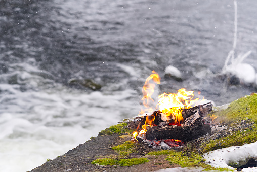 cozy fire on the river bank in winter. small warm bonfire in winter time. campfire by the river on snow an winter season. outdoor holiday concept