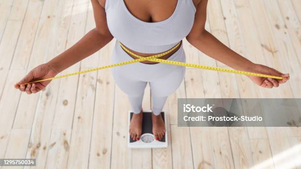 Above View Of African American Lady Measuring Her Waist With Tape Standing On Scales Indoors Closeup Stock Photo - Download Image Now