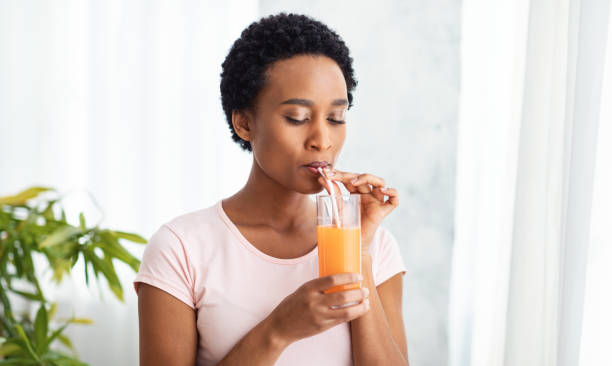Pretty black woman drinking fresh orange juice at home, panorama Pretty black woman drinking fresh orange juice at home, panorama. Slim African American lady having tasty fruit beverage indoors. Healthy living and detox concept juice drink stock pictures, royalty-free photos & images